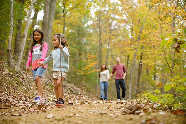 Mom, dad and two little girls hike in the woods in early autumn